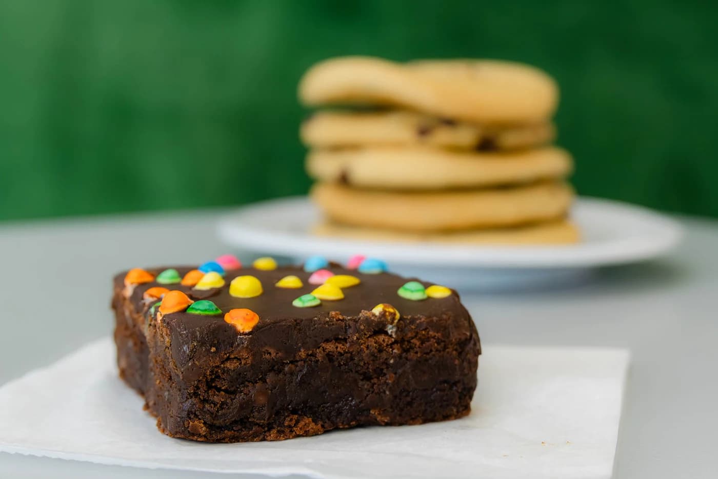 A candy-topped brownie in front of a stack of cookies