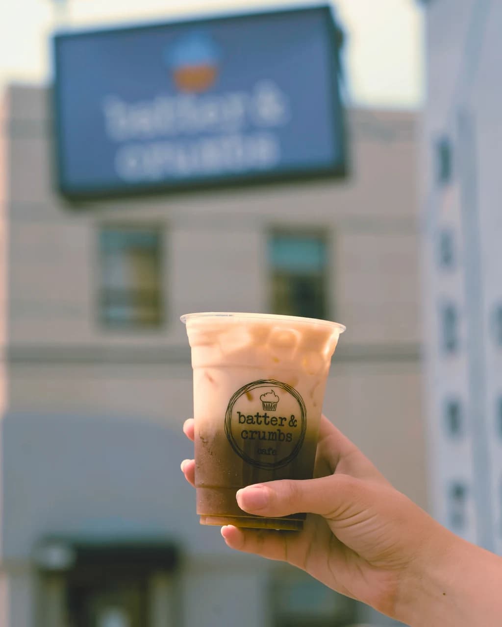 A hand holding an iced coffee outside the shop