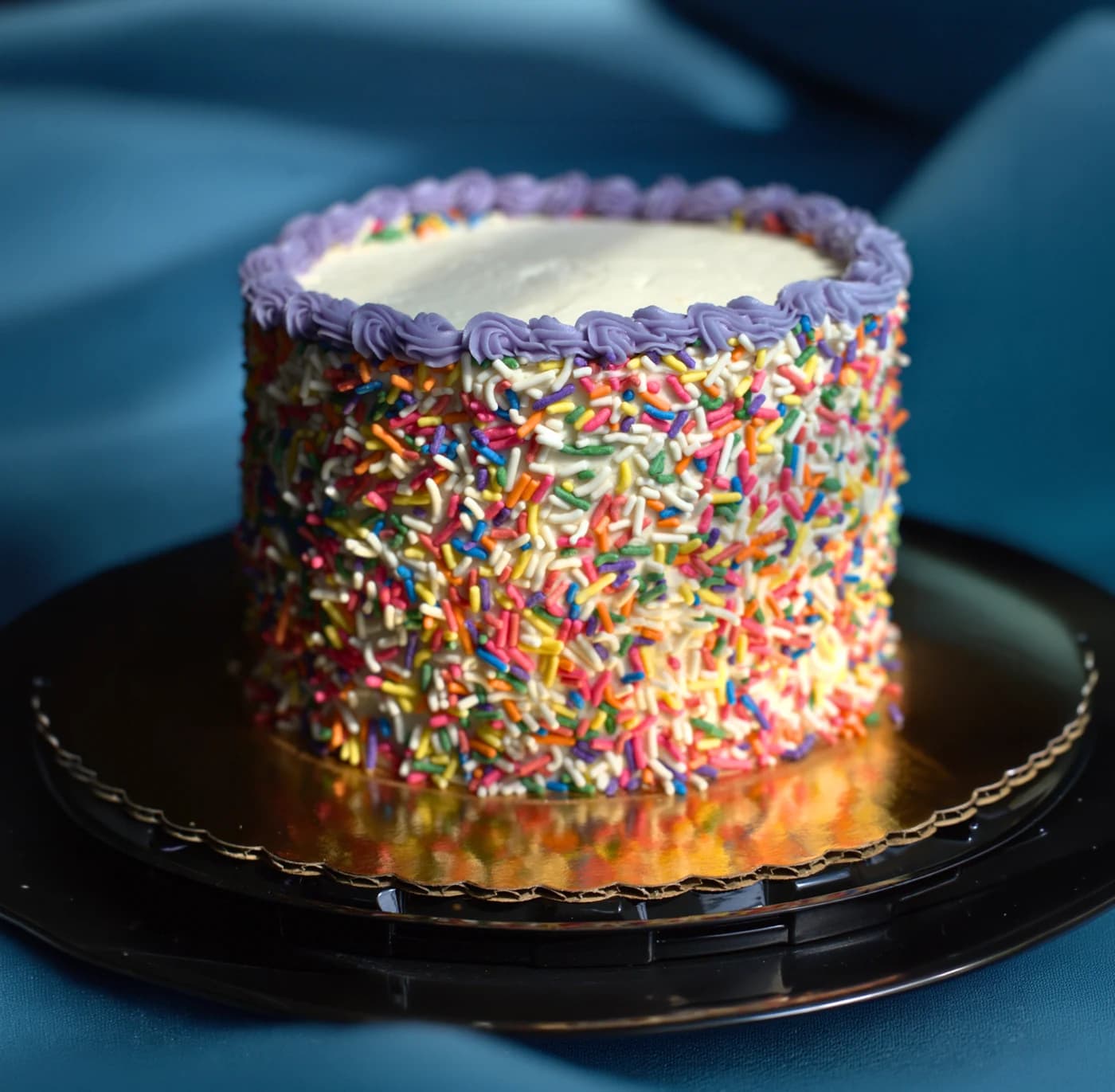 A rainbow sprinkle cake on a black cake stand