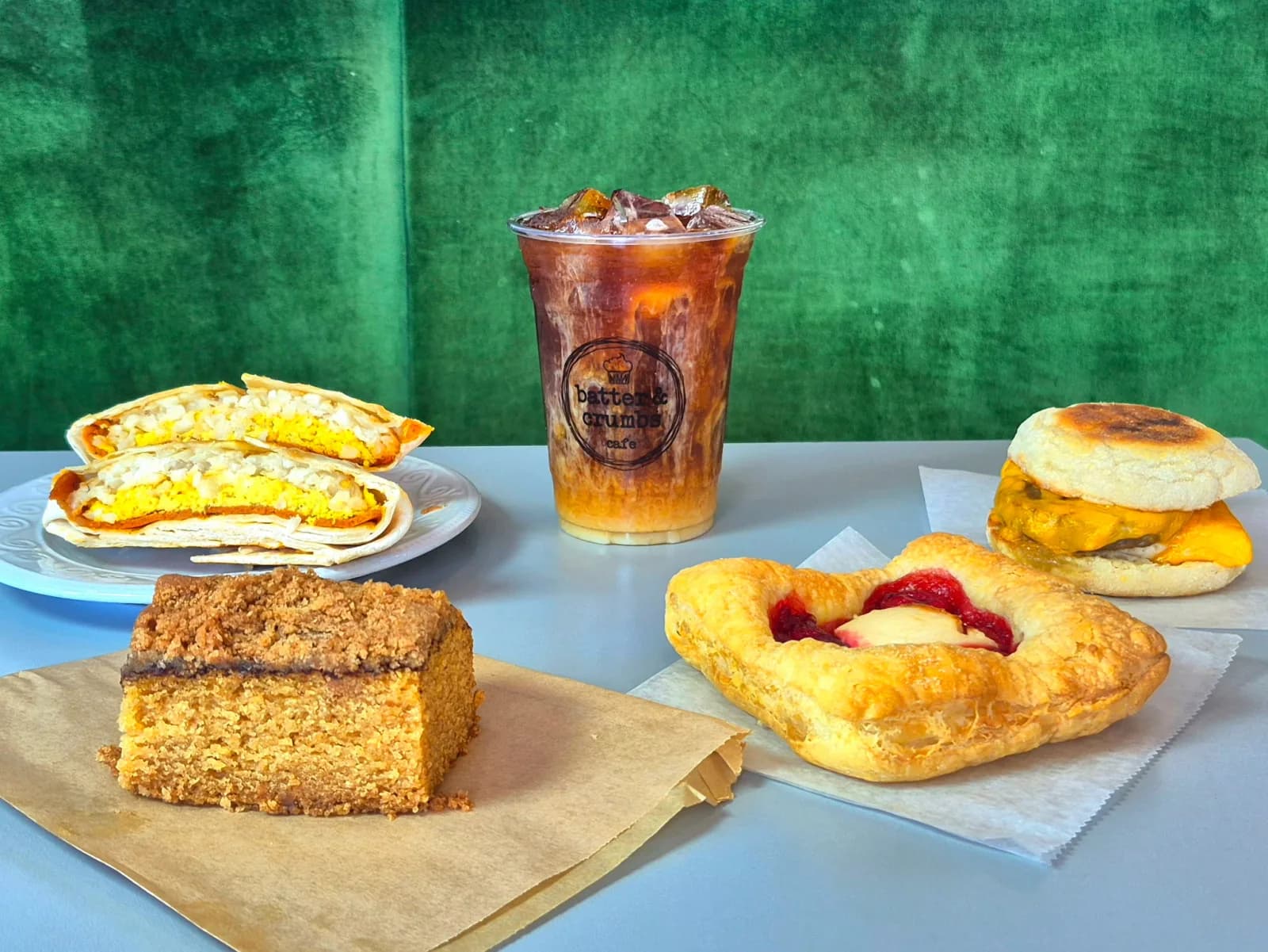 A vegan breakfast spread at Batter & Crumbs — breakfast sandwiches, crumb cake, a fruit danish and an iced coffee