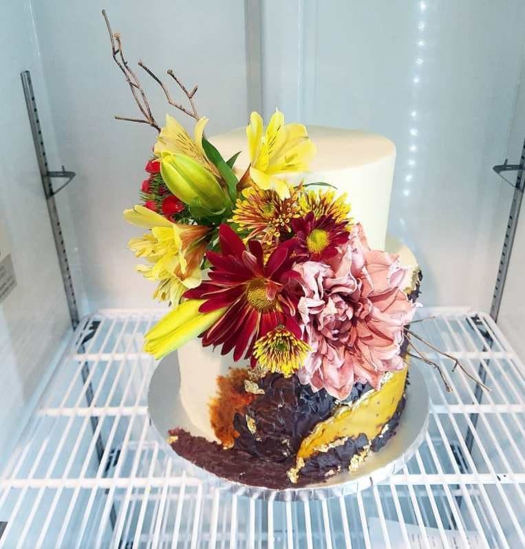 Single-tier vegan wedding cake dressed in fresh florals over a chocolate-and-gold textured base