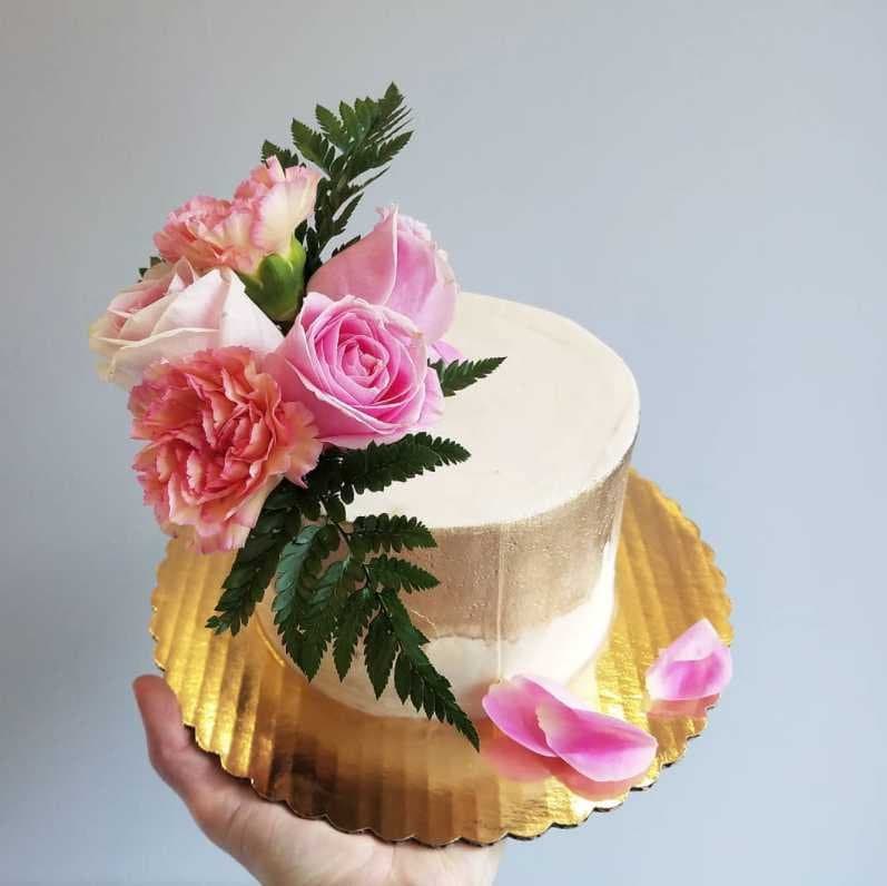 Ivory vegan wedding cake with a gold band, fresh pink roses, and fern